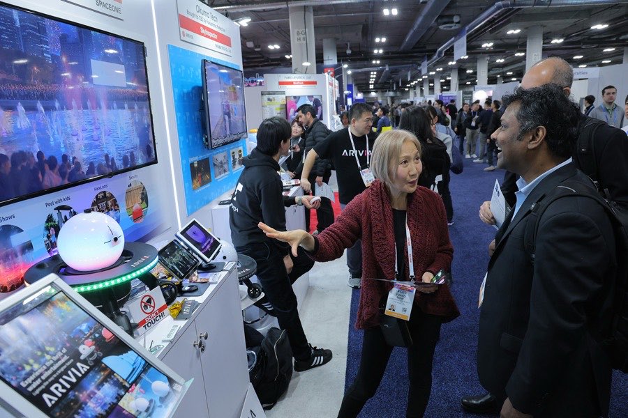 Visitantes conversando no corredor de estandes do CES, com telas e produtos em exposição